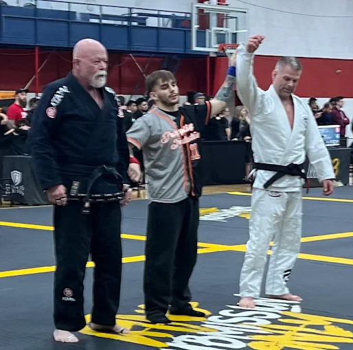 Referee raises a black belt competitor's arm in victory at a BJJ tournament.