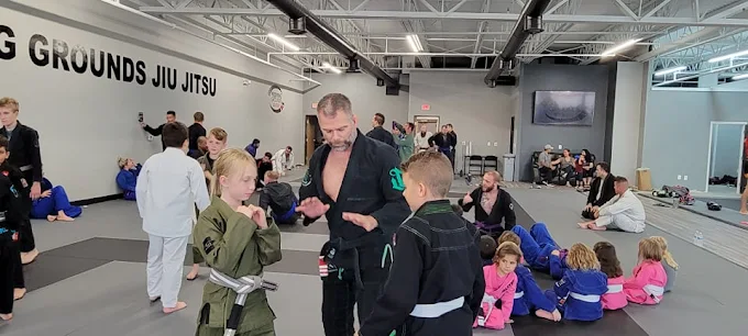 Black belt instructor demonstrating BJJ to kids in gis on the academy mats.